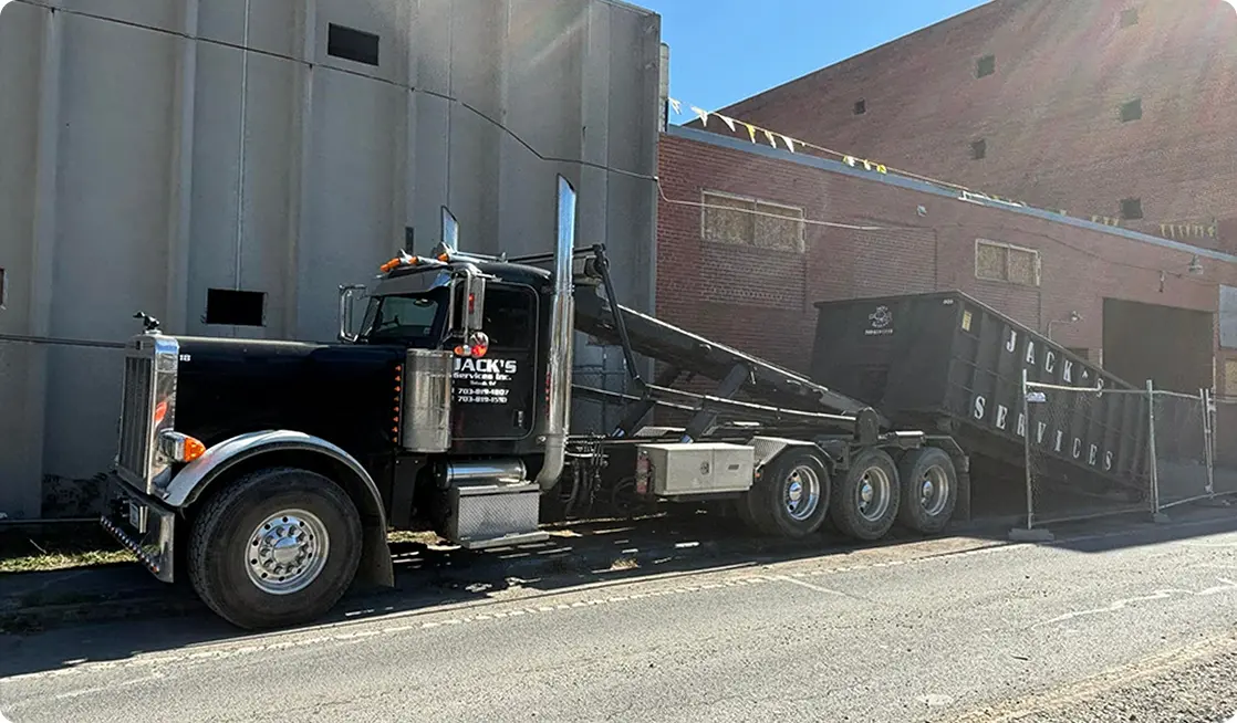 Black truck with dumpster on street.